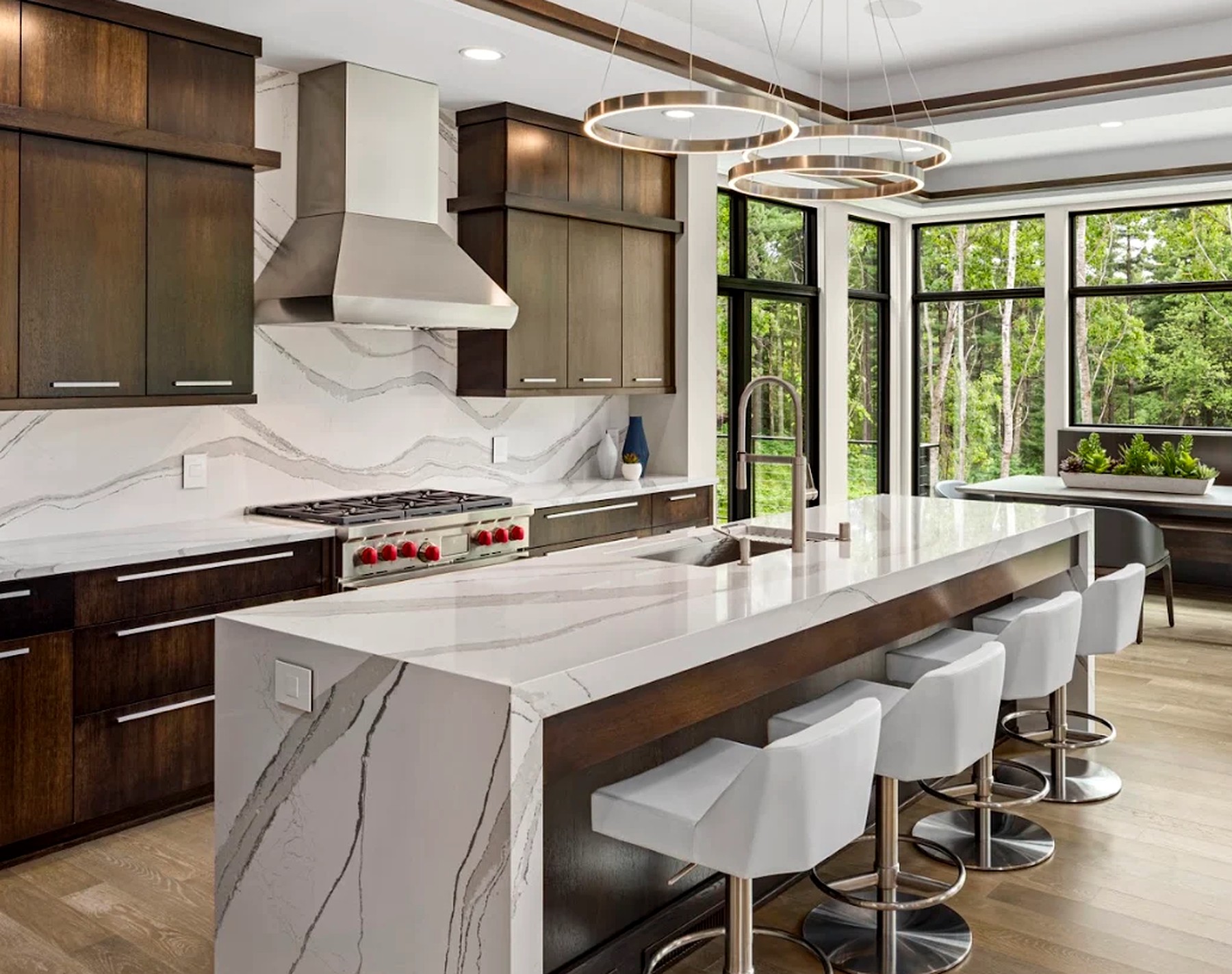 Kitchen with a quartz waterfall island, professional range and stainless hood under walls of windows